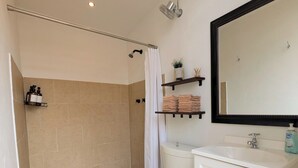 Un baño con ducha, inodoro, lavamanos y espejo.