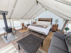 Alojamiento con tienda de campaña, cama, mesa, sofá, cabecero de madera y chimenea.