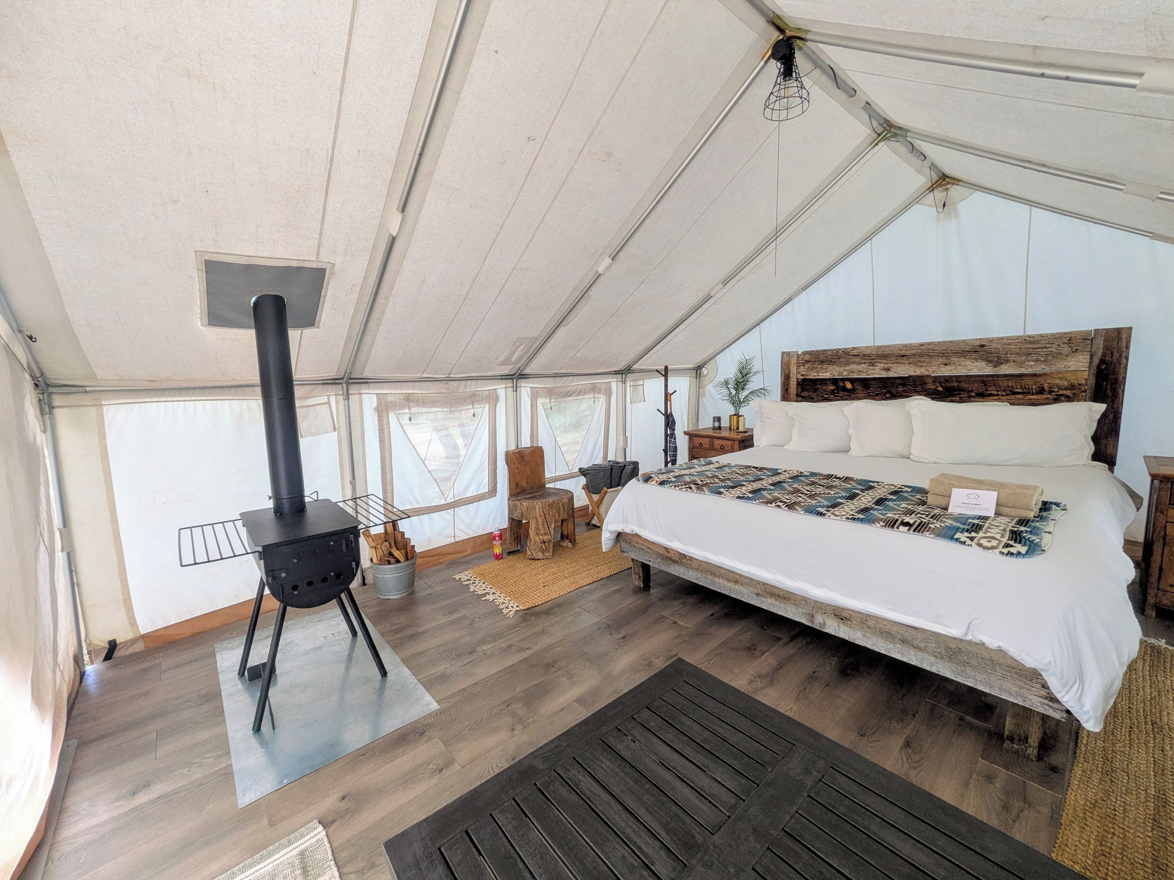 Eine Zelthütte mit Bett, Holzofen und Blick ins Freie.