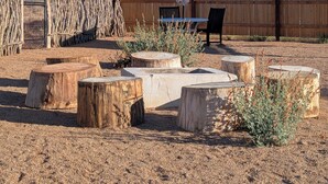 Un patio con mesas y sillas de madera, una valla de madera y una gran formación rocosa al fondo.