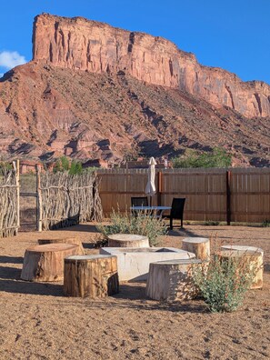 A patio with wooden tables and chairs, a wooden fence, and a large rock formation in the background.