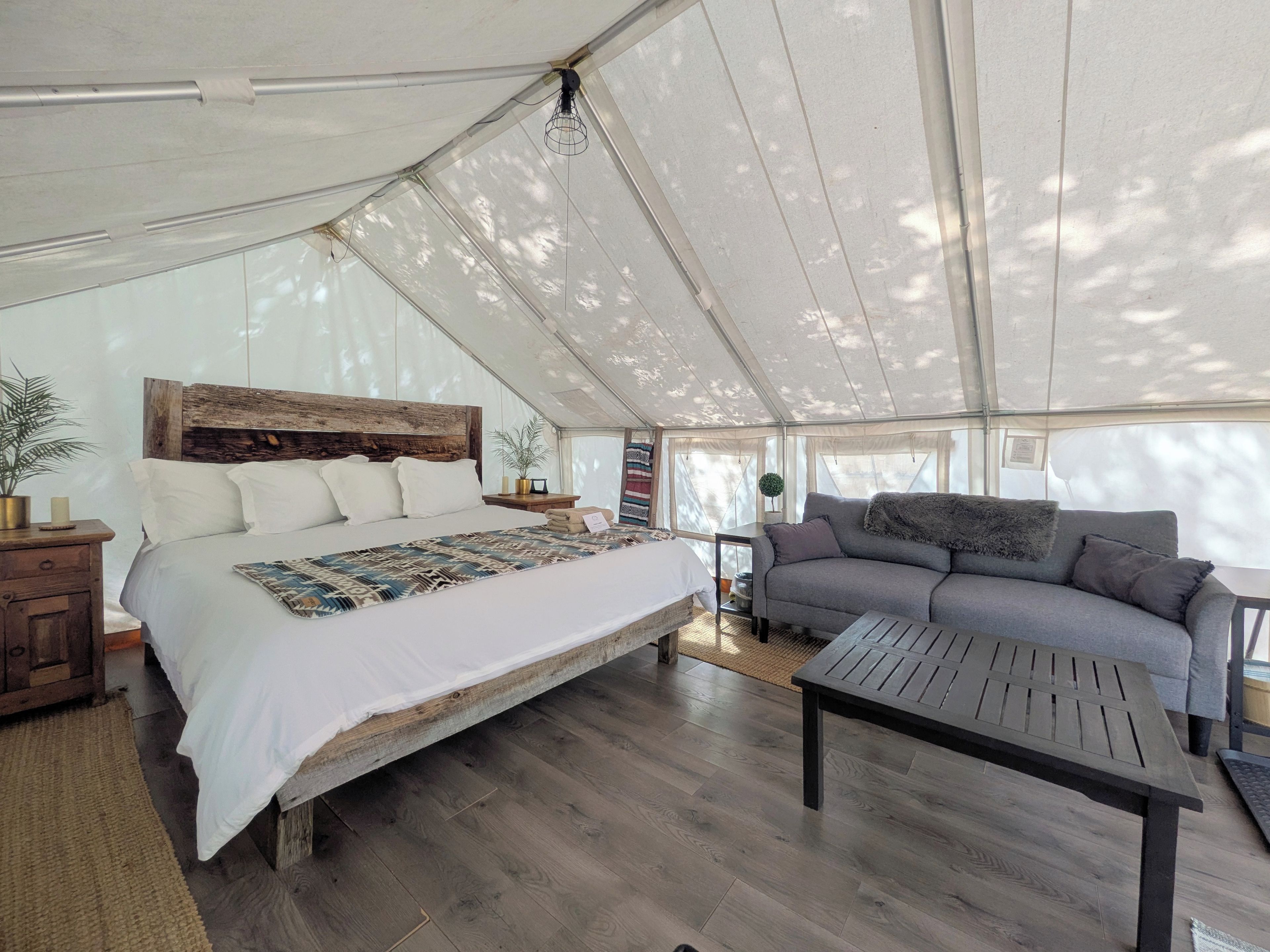 A tented accommodation with a bed, sofa, and table.