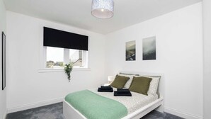 Une chambre à coucher avec un lit, une fenêtre donnant sur un beau paysage, une plante suspendue et un luminaire au plafond.
