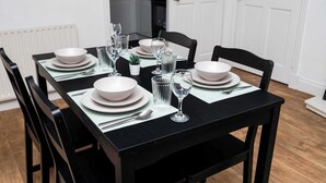 Une table à manger dressée avec des assiettes, des verres et des couverts, entourée de chaises noires.
