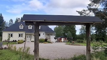 Et hus med grusbelagt indkørsel og en træpergola i forgrunden.