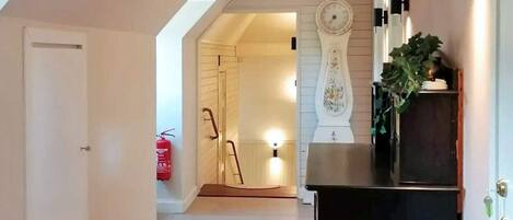 A hallway with a striped rug, a clock, and a fire extinguisher.
