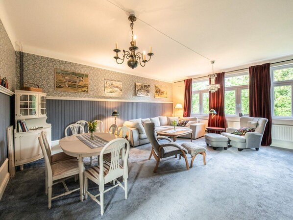A cozy living room with a dining area, featuring a chandelier, a fireplace, and artwork on the walls.