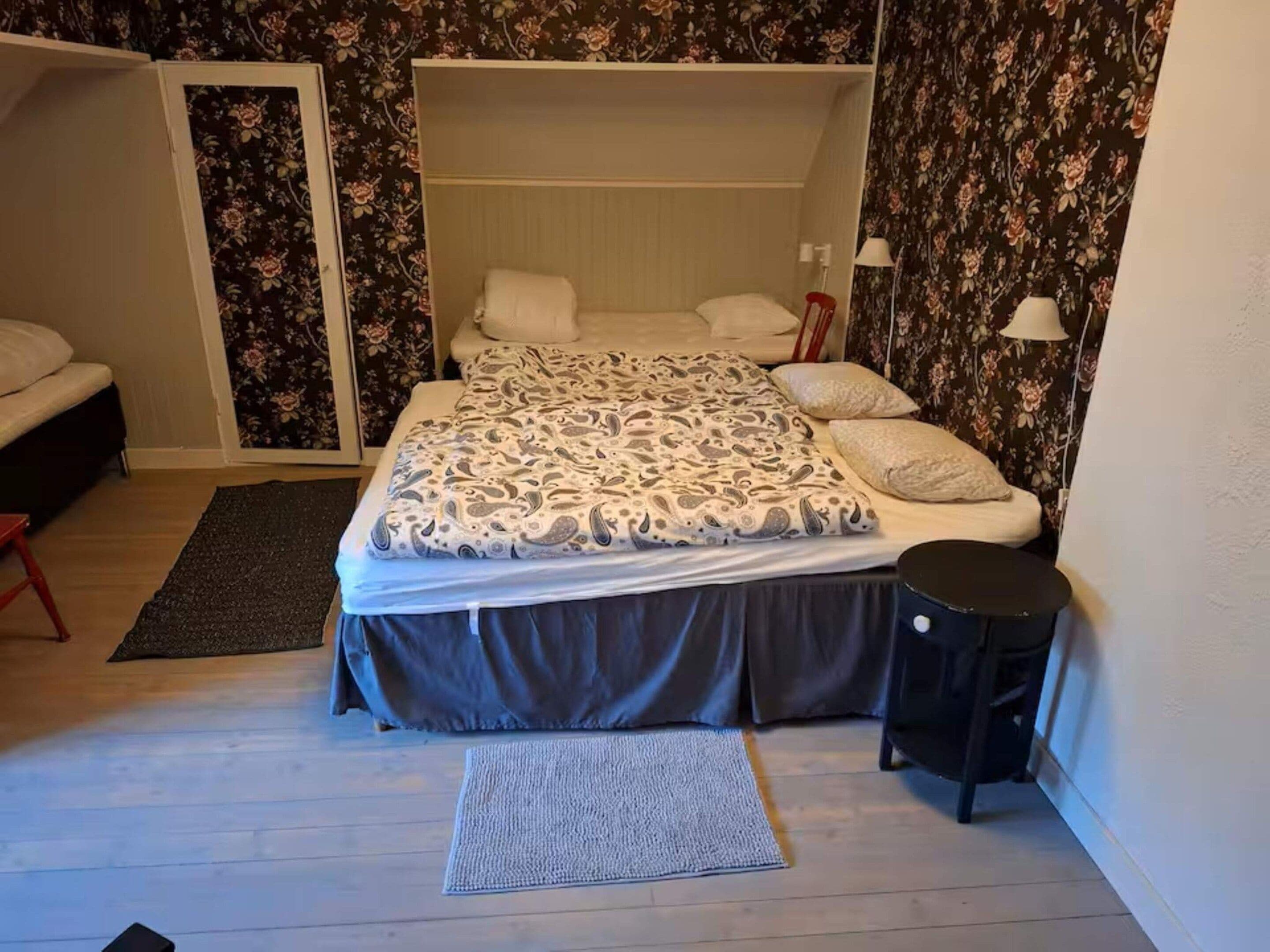 A bedroom with a bed, a small table, a chair, a wardrobe, and a door.