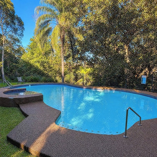 Ein Schwimmbecken mit Kieselsteinkante, umgeben von Gras und Bäumen.