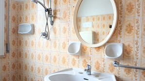 Une salle de bain équipée d’un lavabo, d’un miroir, d’une douche et de deux distributeurs de savon.