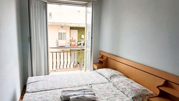 Une chambre à coucher avec un lit, une tête de lit en bois et un balcon donnant sur un immeuble.