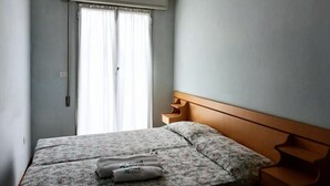 Une chambre à coucher avec un lit, une fenêtre avec des rideaux, un climatiseur fixé au mur et une tête de lit en bois.