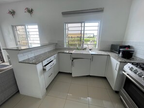 A kitchen with white cabinets, a granite countertop, a sink, a microwave, a stove, and a window with a view of greenery. - Top floor Oasis/Private Pool/ High-Speed WiFi (Punta Cana)