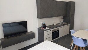 Une chambre d’hôtel compacte équipée d’une télévision à écran plat, d’une kitchenette, d’une petite table à manger et d’un lit.