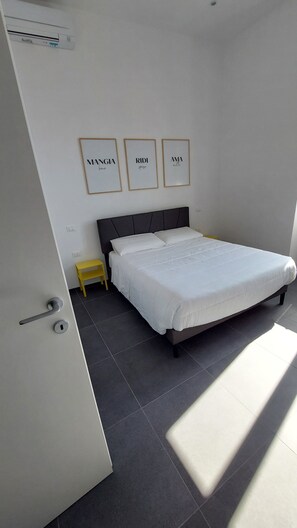 Un dormitorio moderno con una cama grande, una mesita de noche pequeña y tres frases motivacionales enmarcadas en la pared.