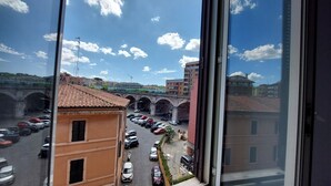 Une vue à travers une fenêtre sur une rue où sont garées des voitures, un pont et des immeubles, avec un ciel dégagé.