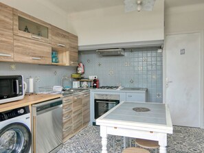Eine kleine Küche mit Holzschränken, einer Mikrowelle, einem Geschirrspüler, einem Gasherd und einem kleinen Tisch.