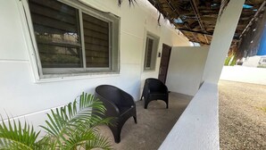 Un espace extérieur abrité comprenant deux chaises, une plante en pot et un bâtiment doté d’une fenêtre et d’une porte.