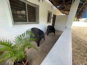 A covered outdoor area with two chairs, a potted plant, and a building with a window and door. - Downstairs Oasis/Private Pool/ High-Speed WiFi (Punta Cana)