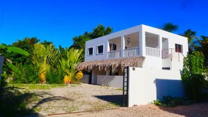 Un bâtiment blanc avec un toit de chaume, un balcon et une échelle menant à l’entrée.