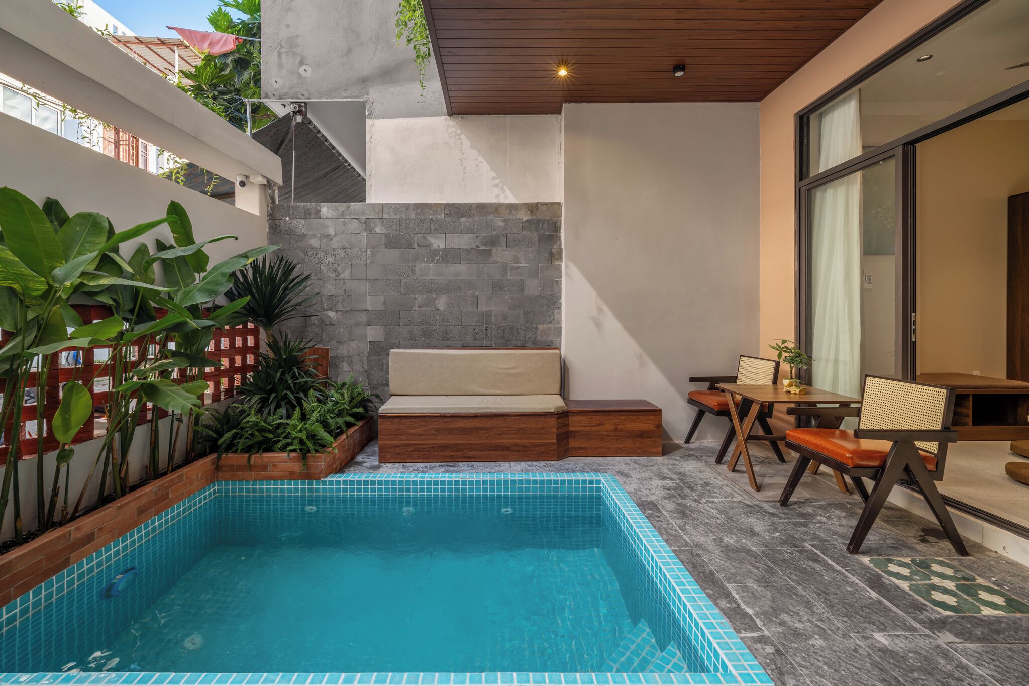 A swimming pool with a tiled edge, a wooden deck, and a seating area with a bench and chairs.