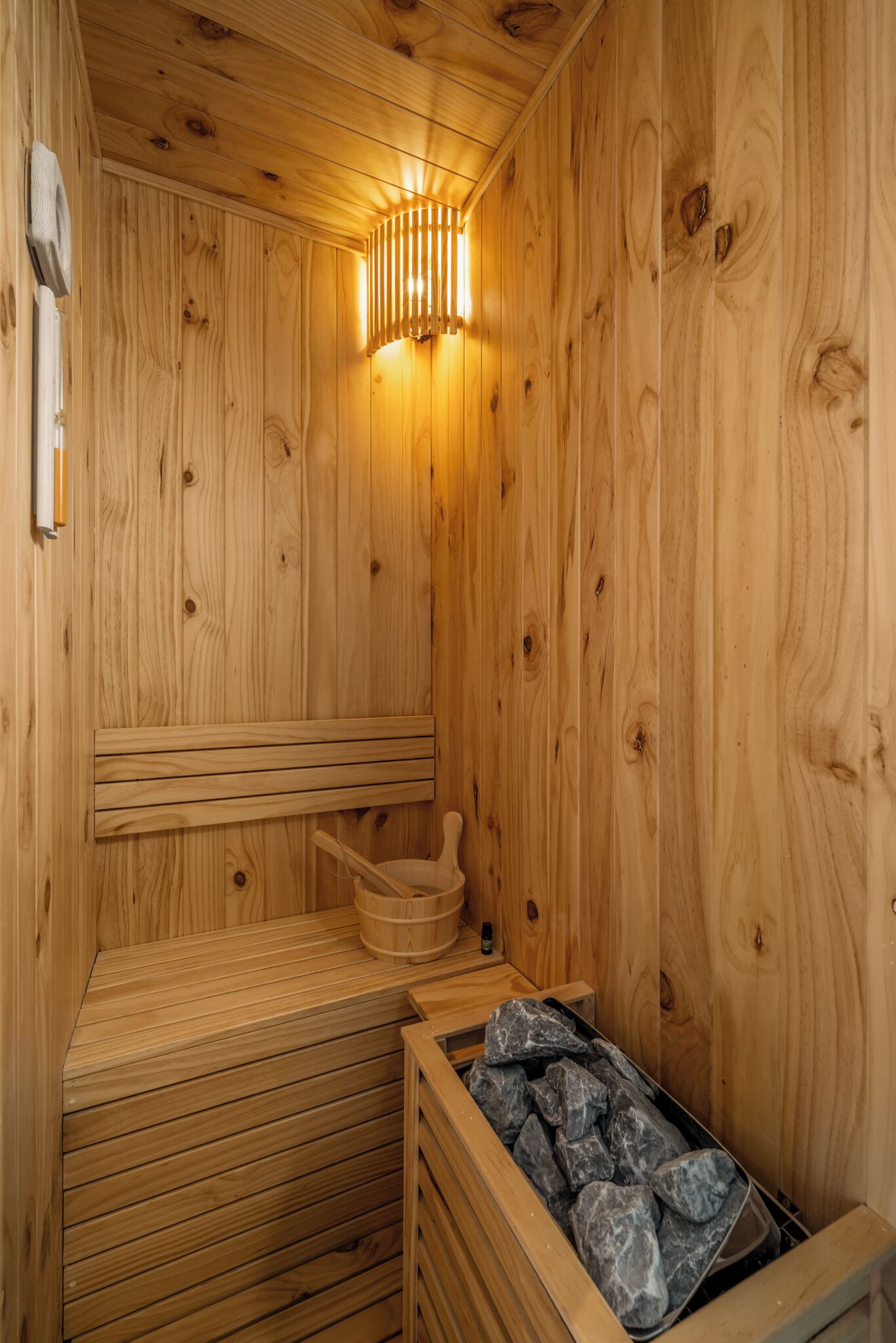 Een houten sauna met een bank, een stenen wasbak en een bak met stenen.