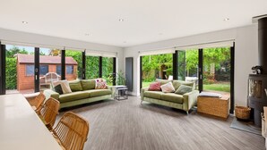 A spacious living room with two green sofas, a dining table with wicker chairs, and a fireplace. - New! Central 3BR near Kenilworth Castle and A46 (Kenilworth)