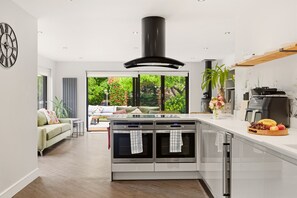 Eine moderne Küche mit einer zentralen Kochinsel, zwei Backöfen und einem großen Fenster mit Blick auf einen Garten.