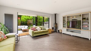 A spacious living room with a sofa, TV, and entertainment unit, large windows, and a fireplace. - New! Central 3BR near Kenilworth Castle and A46 (Kenilworth)