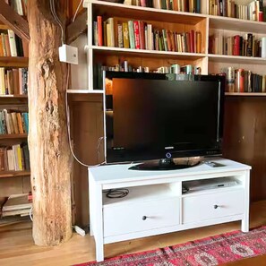 A white entertainment center with a flat-screen TV, wooden bookshelves, and a large tree trunk.