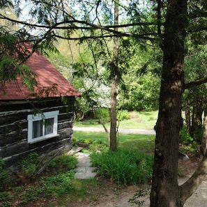 A rustic log cabin with a red roof, surrounded by greenery and a stone pathway.