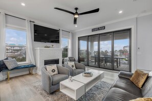 A modern living room with a fireplace, two grey sofas, a white coffee table, and a large sliding glass door to the outside. - The White House Pool Oceanviews! Rooftop Deck (New Smyrna Beach)