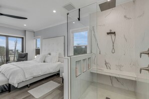 A modern bedroom with a large bed, a glass-enclosed shower, and a view through the window. - The White House Pool Oceanviews! Rooftop Deck (New Smyrna Beach)
