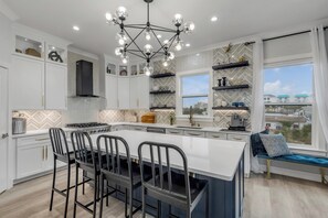A modern kitchen with a central island, pendant lighting, and a view through the window. - The White House Pool Oceanviews! Rooftop Deck (New Smyrna Beach)