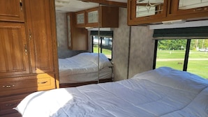 A bedroom with two beds, wooden cabinets, and a window with a view of a grassy area.