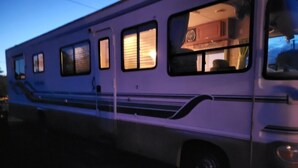 A white RV with multiple windows, a kitchen area visible through the windows, and a side step.