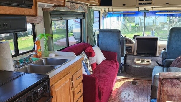 An RV interior with a kitchen, a seating area, and a window providing a view of the outdoors.