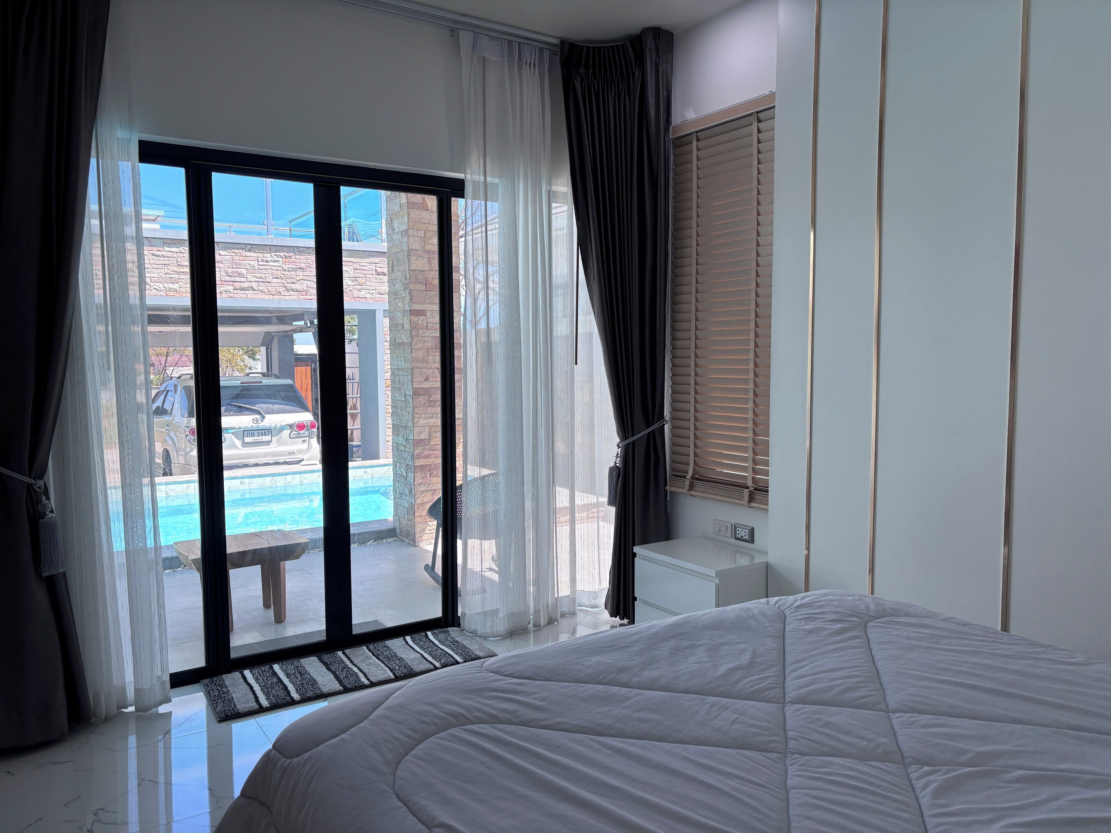 A bedroom with a large bed, a sliding glass door leading to a pool area, and a view of the outside.