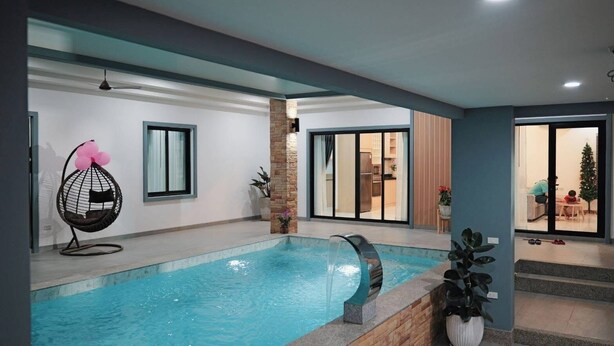 An indoor swimming pool with a stone wall, a hanging chair, and a view of the living area through glass doors. - Luxury 3-bedroom Pool Villa in peaceful Hua Hin (Hua Hin)