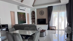A modern living room with a marble floor, a large flat-screen TV, a dining table with chairs, a sofa, and a ceiling fan. - Luxury 3-bedroom Pool Villa in peaceful Hua Hin (Hua Hin)