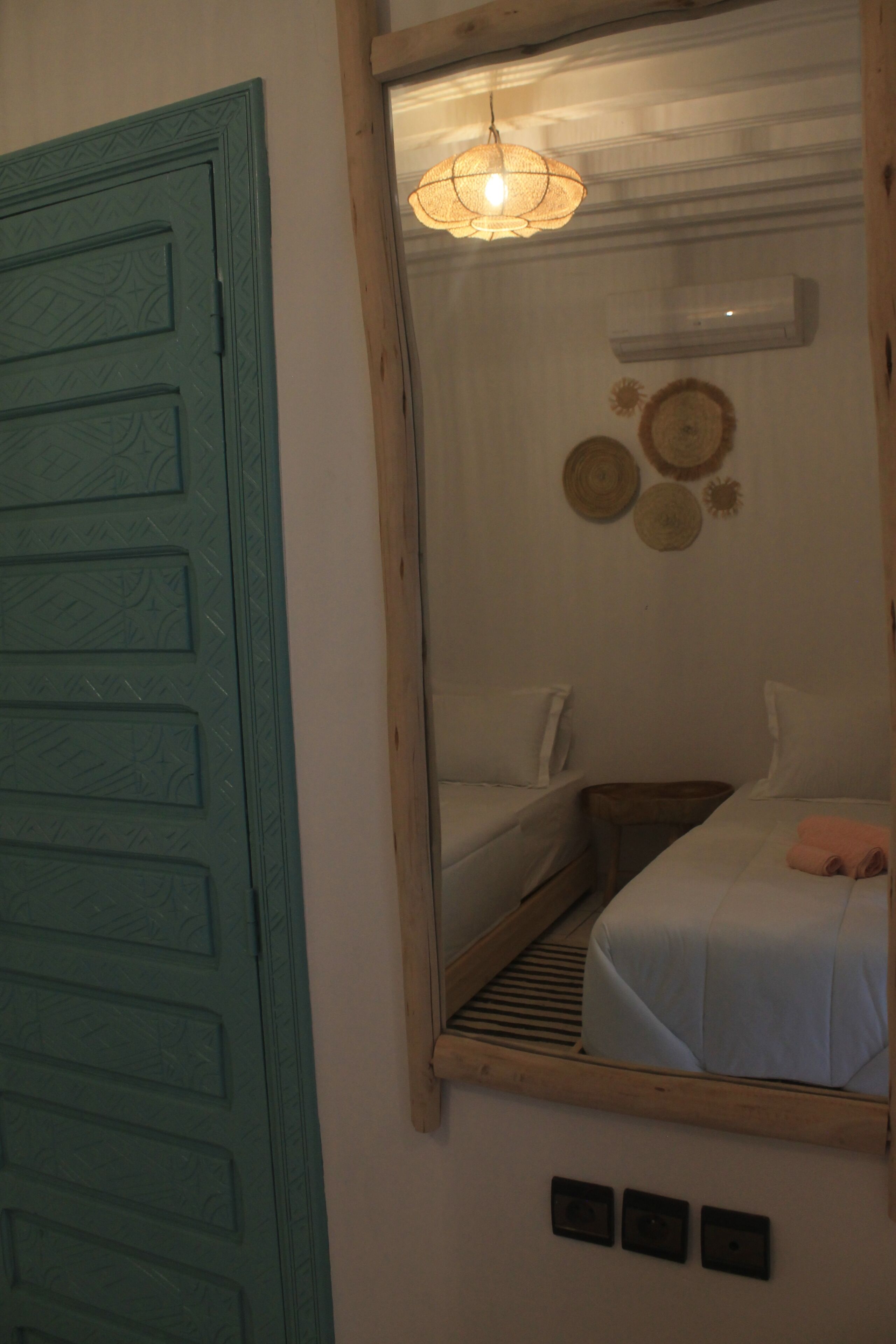 Een kamer met een bed, een spiegel, een lamp en een deur.