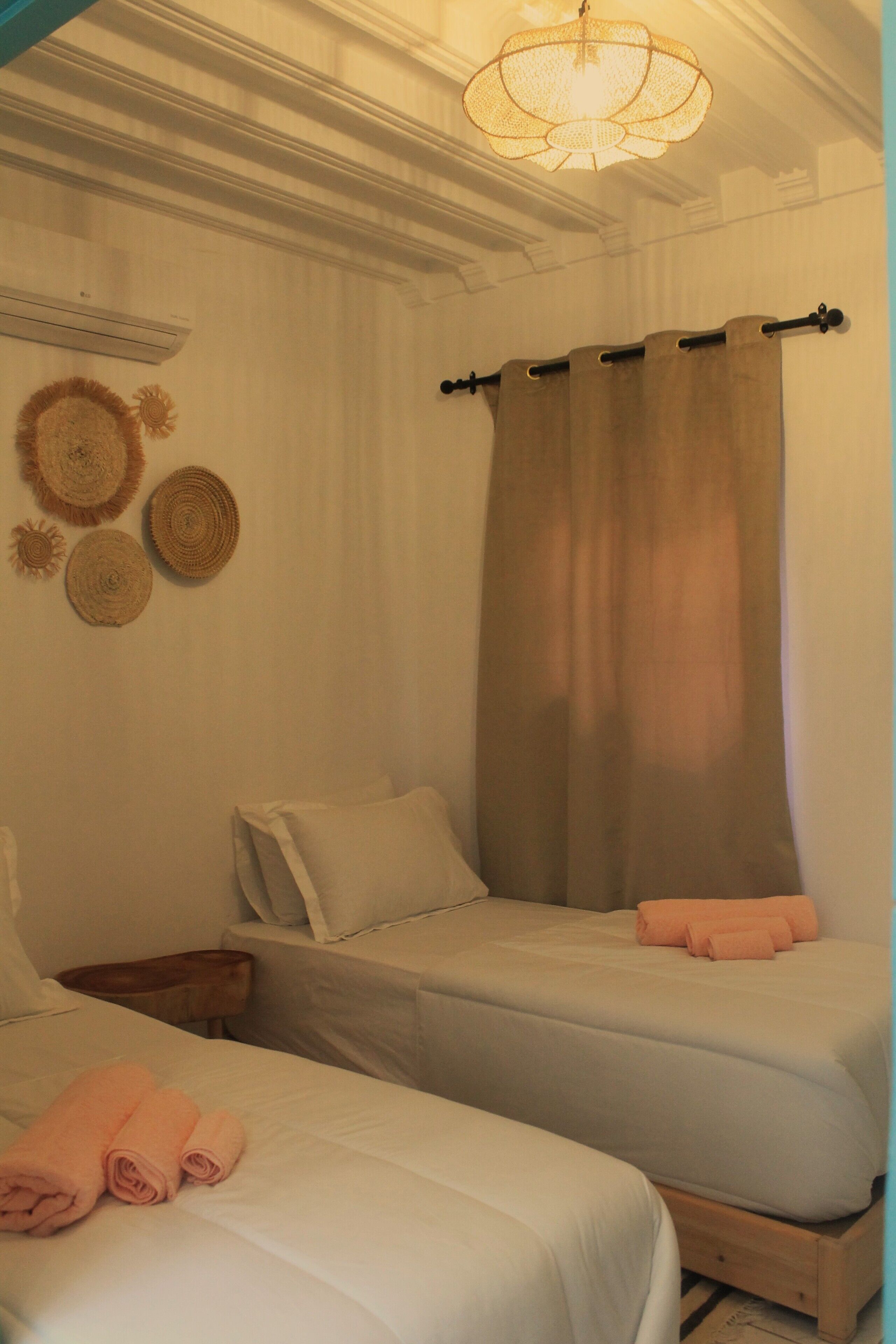 A room with two beds, a wooden nightstand, a wall-mounted air conditioner, and a ceiling light fixture.