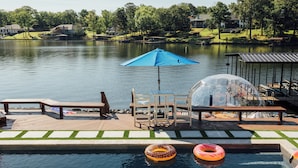 A pool area with a wooden deck, lounge chairs, a table, and a blue umbrella. - The Superstar | Waterfront Pool & Pickleball (Hot Springs National Park)