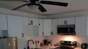 Een moderne keuken met witte kastjes, roestvrijstalen apparatuur, een plafondventilator en een magnetron.