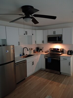 Una cocina moderna con armarios blancos, electrodomésticos de acero inoxidable, ventilador de techo y microondas.