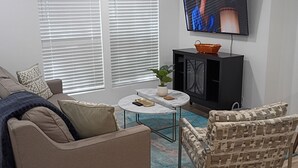 Een woonkamer met een bank, fauteuil, salontafel, televisie en een kast.