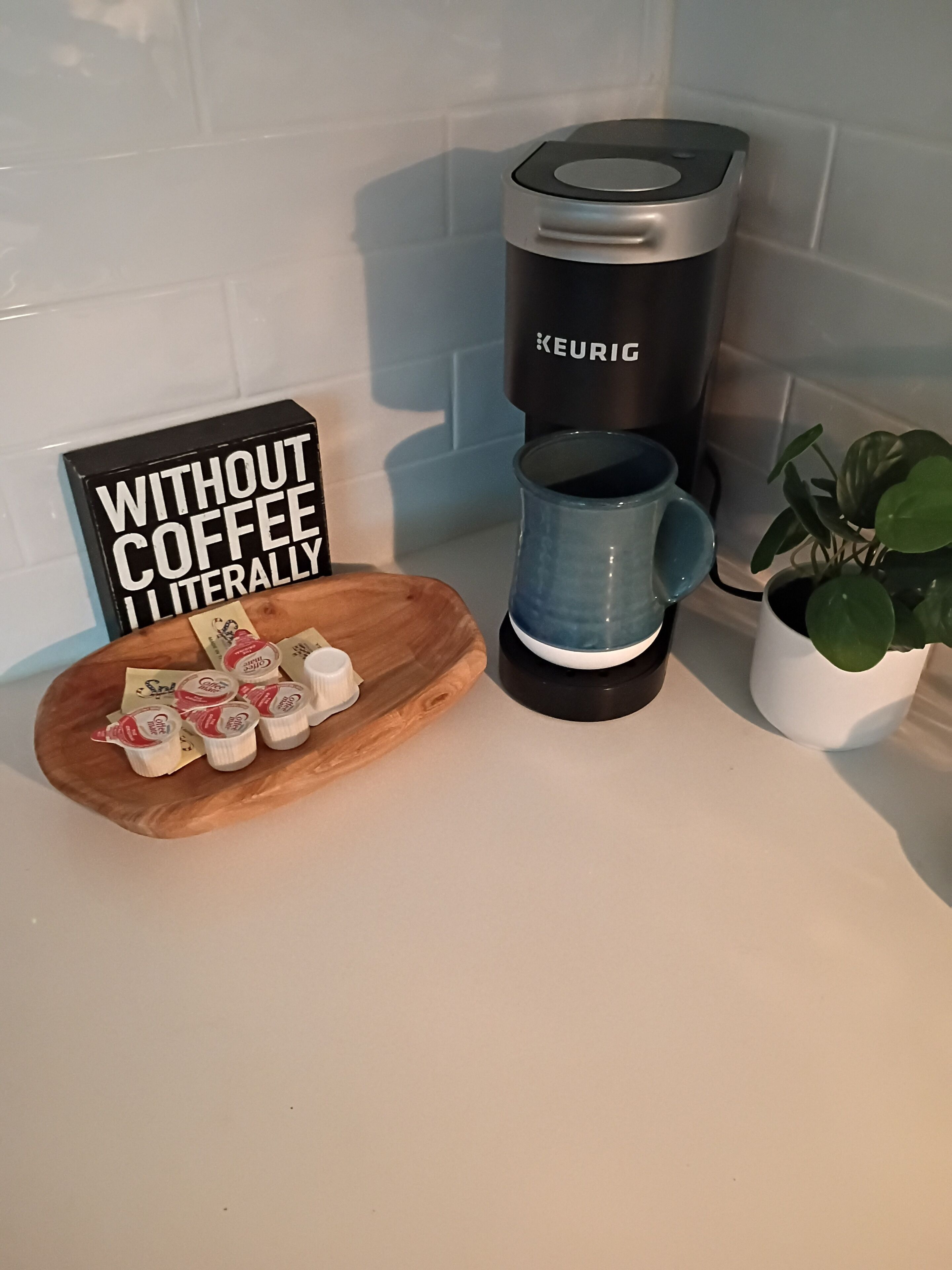 A Keurig coffee maker, a blue mug, a wooden board with coffee pods, and a sign saying 'WITHOUT COFFEE LITERALLY'.