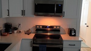 Een keuken met witte kastjes, een oven van roestvrij staal, een magnetron en een broodrooster.