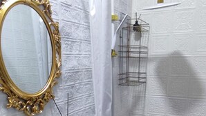Un baño con lavamanos pedestal, espejo con marco dorado, ducha con cortina blanca y pared de azulejos blancos.