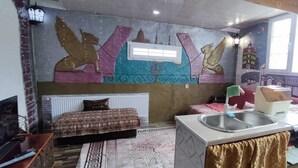 Una habitación compacta con cama, una kitchenette pequeña, una ventana y un mural en la pared.